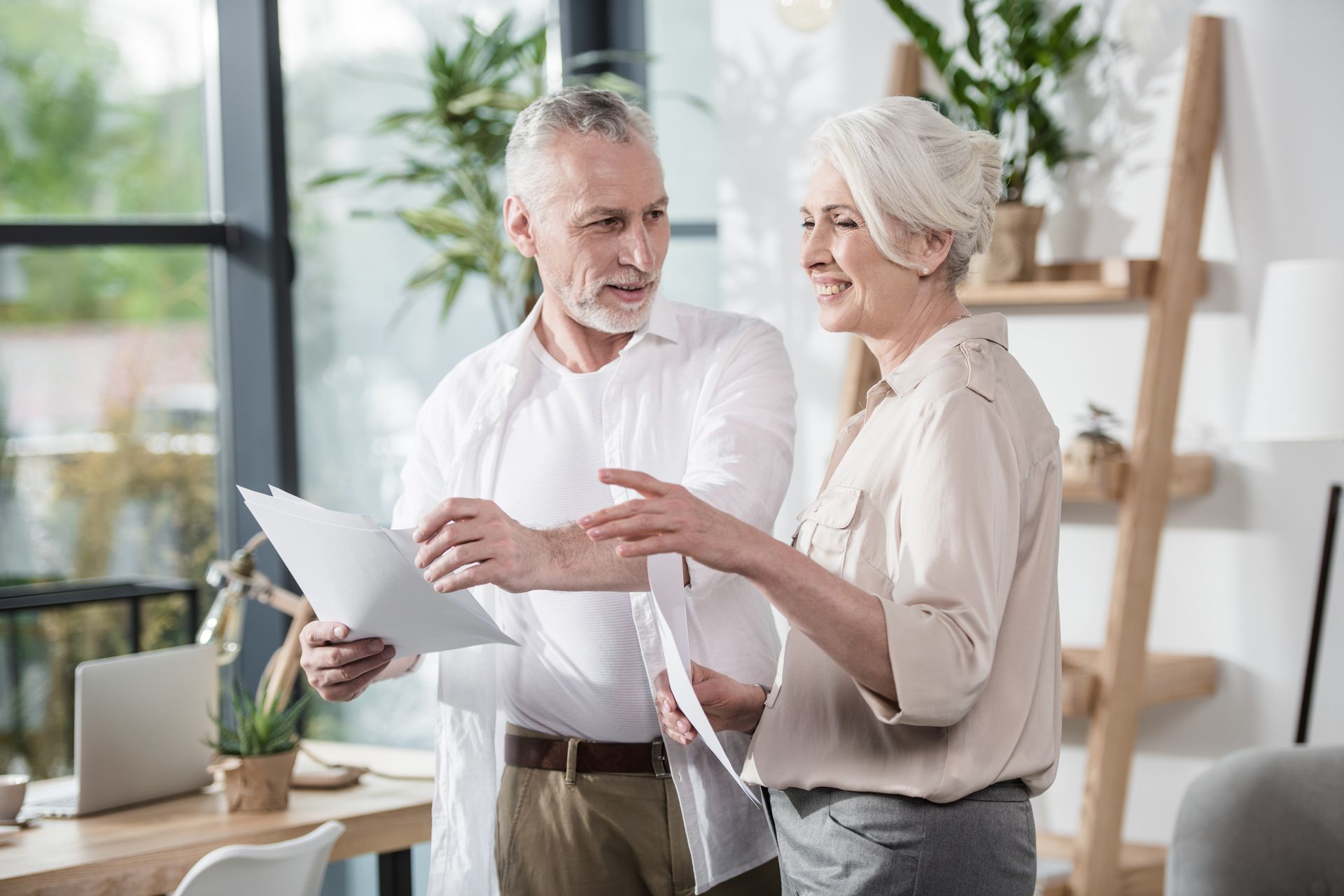Two coworkers discussing documents in a bright office, one holding papers and gesturing while the other listens.