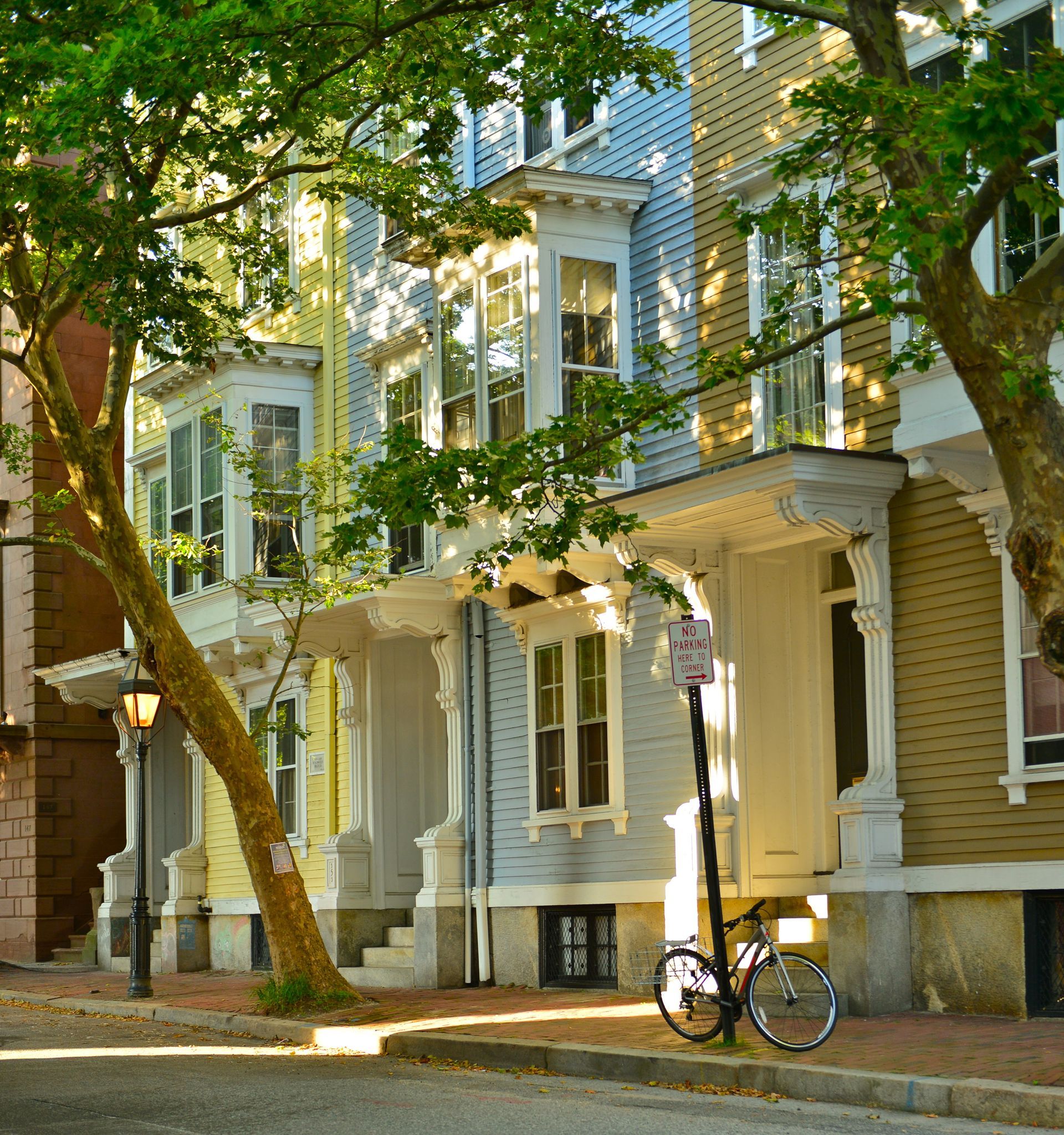 Tree-lined street with a yellow townhouse and a bicycle parked on the sidewalk