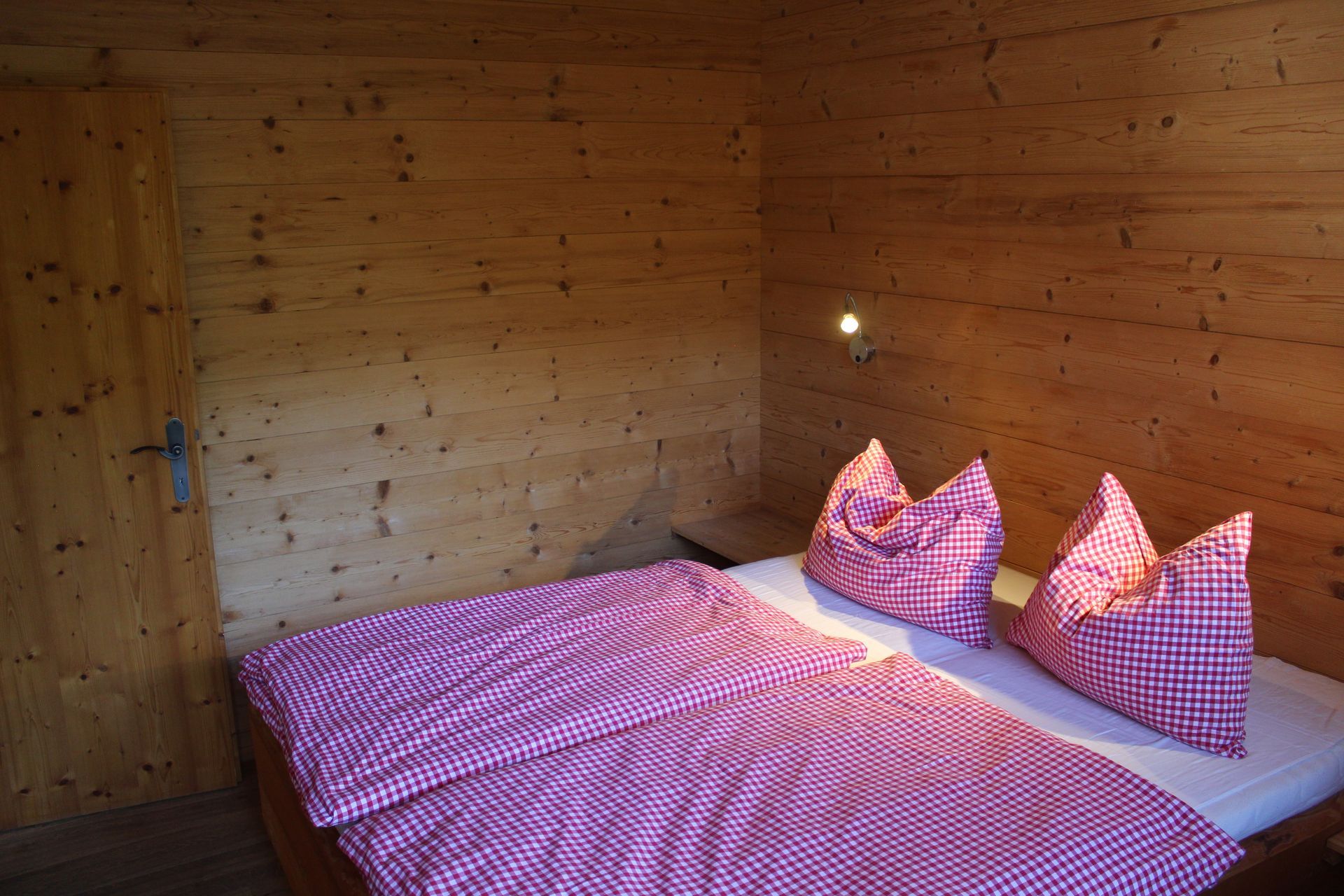 Ein Schlafzimmer mit Holzwänden, in dem ein Bett mit einem rosa-weiß karierten Bettbezug und zwei passenden Kissen steht.