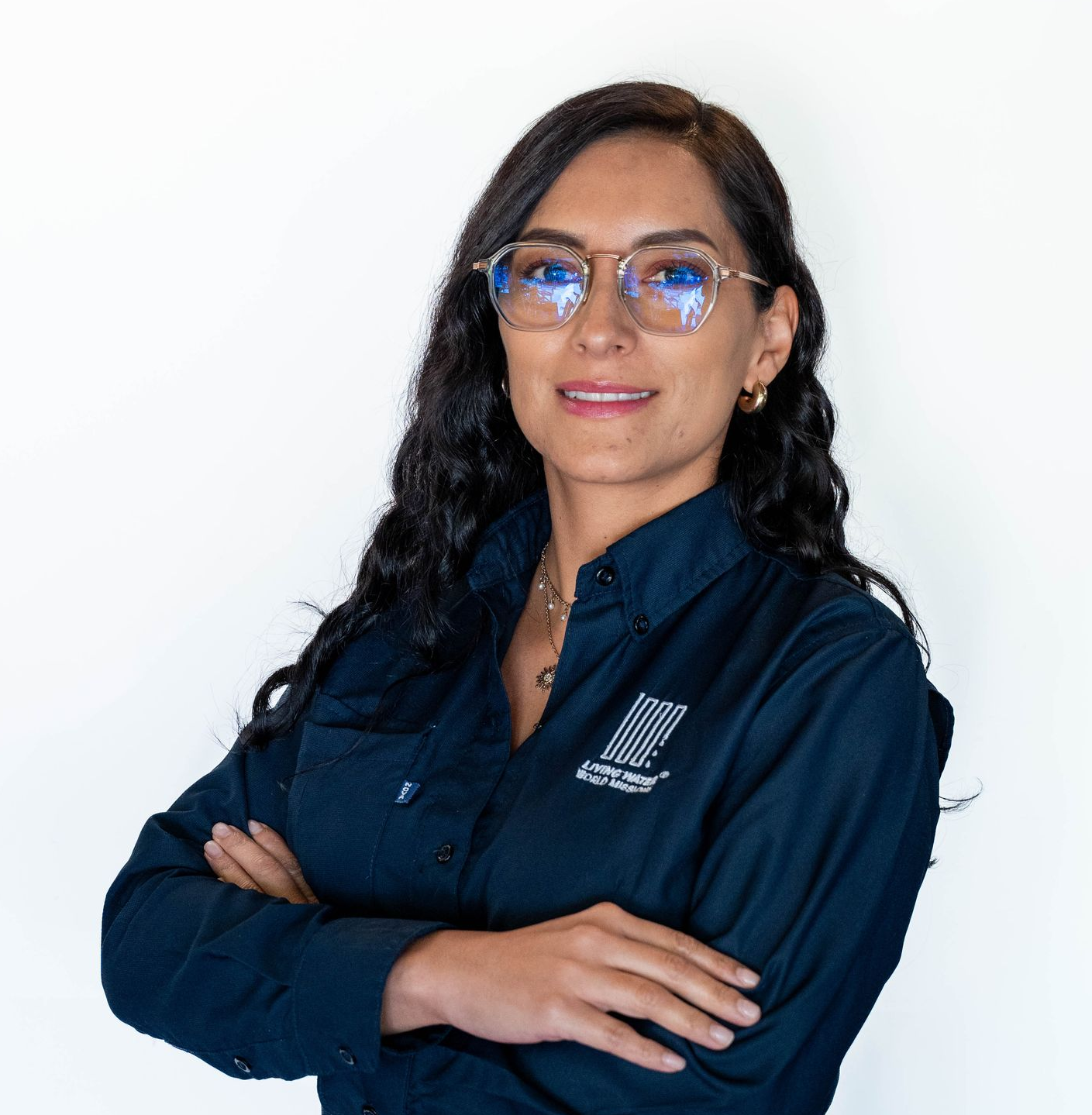 Smiling person with long dark hair and glasses in a light button-up shirt against a gray background