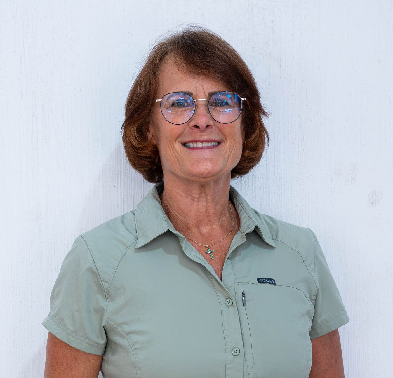 Smiling woman with short brown hair outdoors under leafy shade
