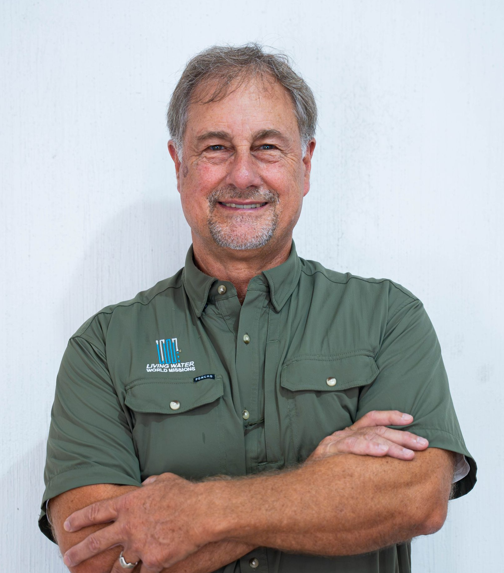 Smiling man in a light gray zip-up shirt against a textured white wall