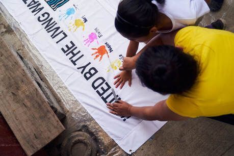 Two people painting colorful text on a white banner laid on the ground