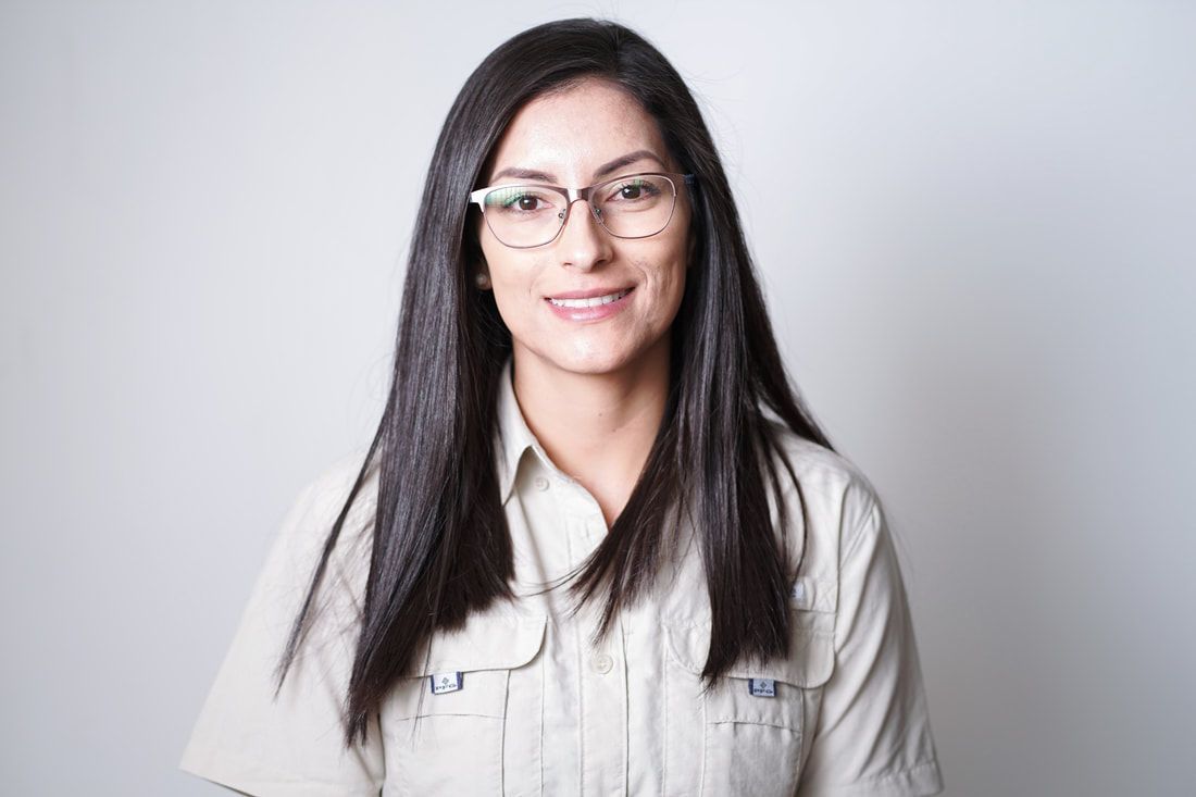 Smiling person with long dark hair and glasses in a light button-up shirt against a gray background