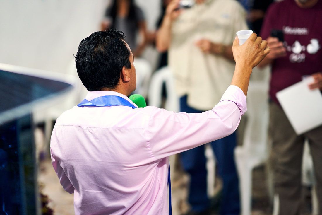 Person in pink shirt raising a hand toward a group indoors, holding a white object.