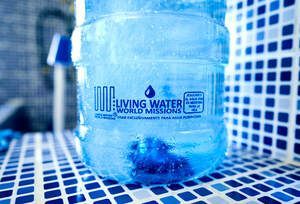 Blue-tinted water bottle with “Living Water” label on a blue tiled surface