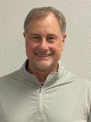 Smiling man in a light gray zip-up shirt against a textured white wall