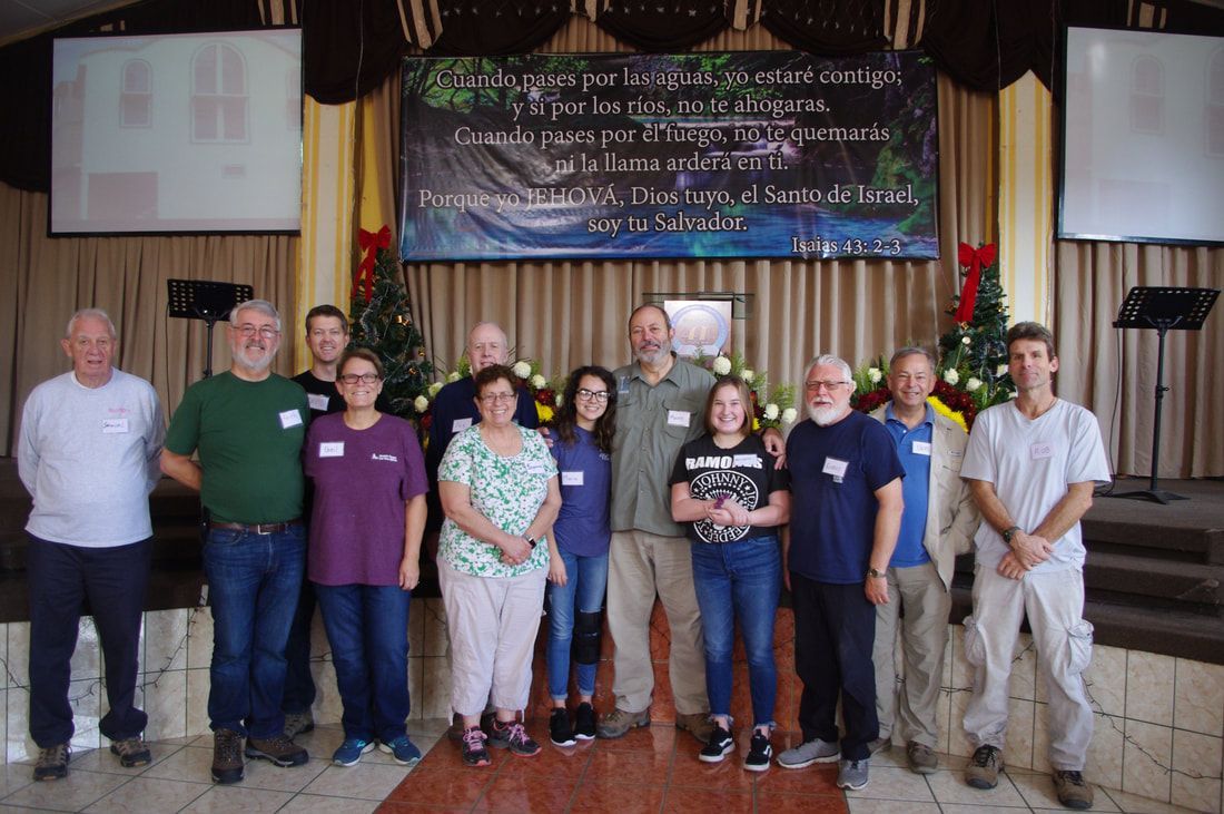 Group of people posing indoors on a stage with a banner and flags behind them
