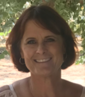 Smiling woman with short brown hair outdoors under leafy shade
