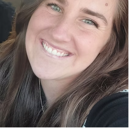 Smiling woman with long brown hair and green eyes, wearing a dark top, close-up portrait