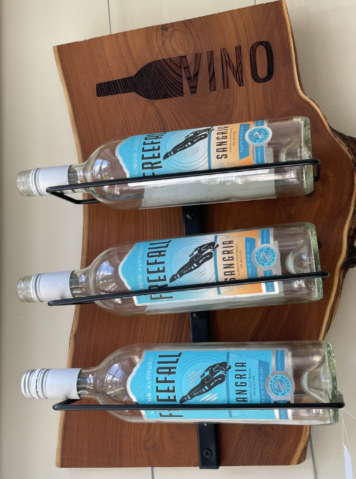 Three bottled wines in a wooden tray on a white surface, one bottle in clear, two in blue labels.