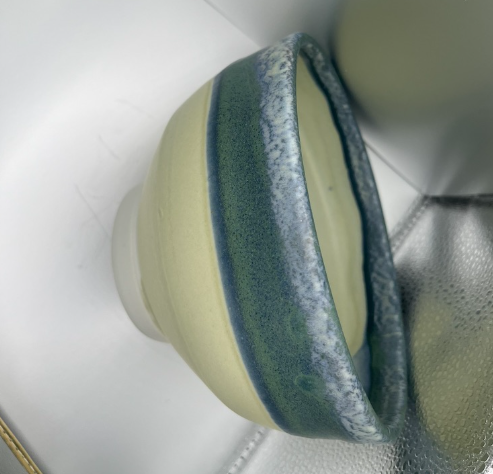 Blue and cream striped ceramic vessel with a rounded base on a metallic surface