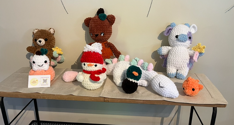 Knitted animal plushies and small crafts displayed on a wooden table against a plain wall.