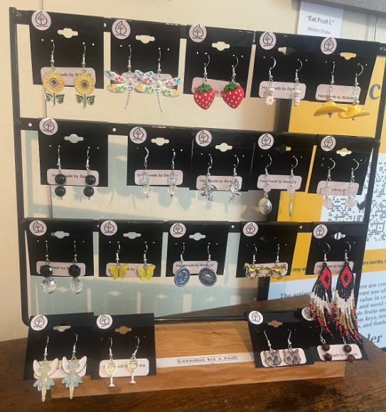 Display of colorful handmade earrings on a black tiered jewelry stand in a shop