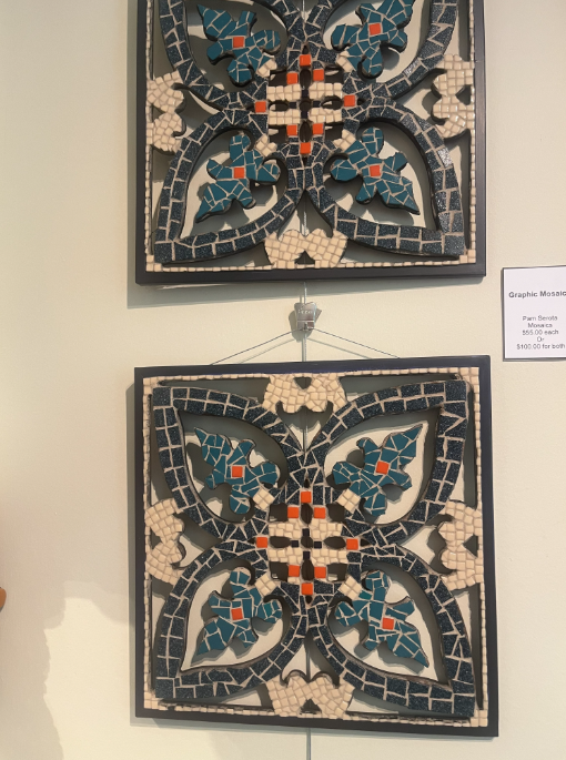 Two framed floral mosaic tiles with dark backgrounds and teal, cream, and orange patterns on a wall.
