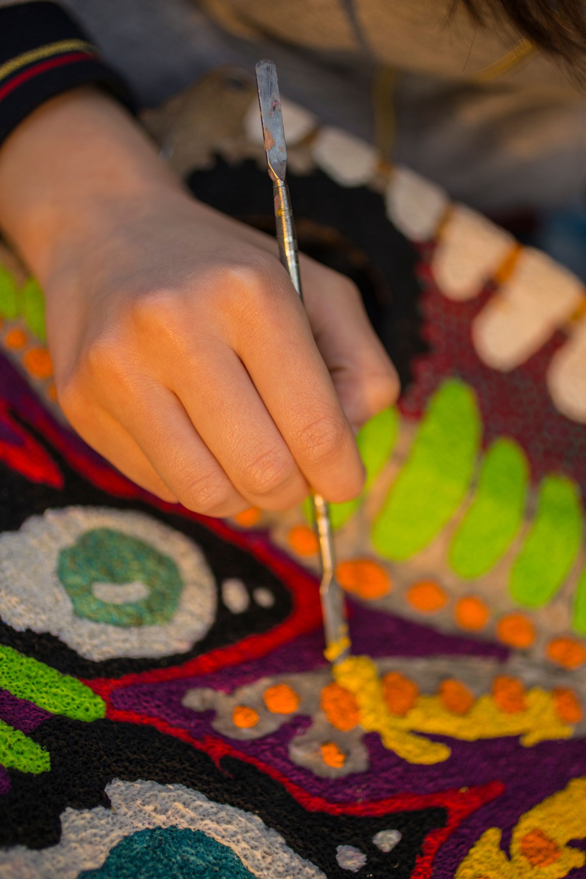 Hand decorating a colorful embroidered fabric with a needle and thread