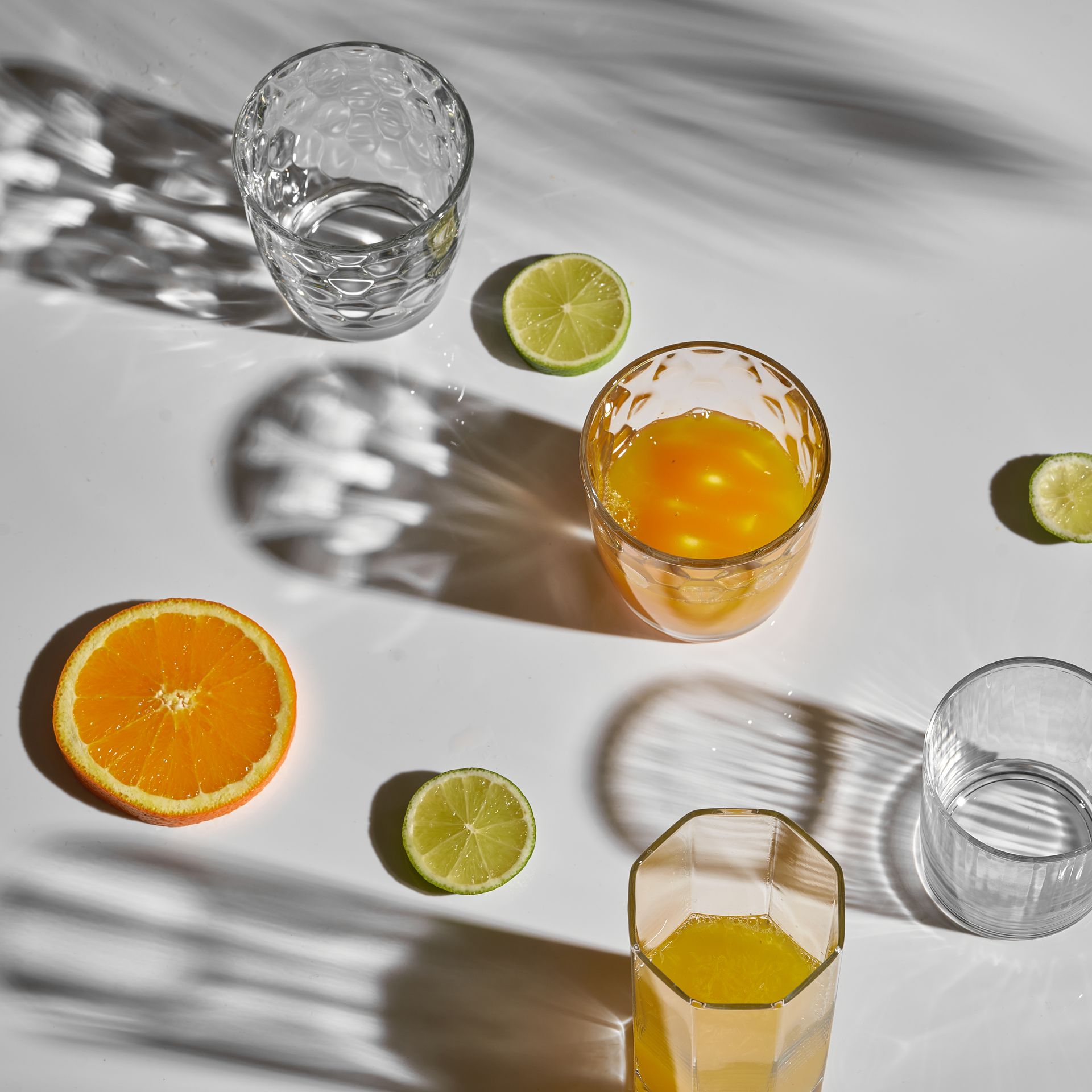 Assorted citrus slices and glasses with orange and lime drinks on a sunlit white surface