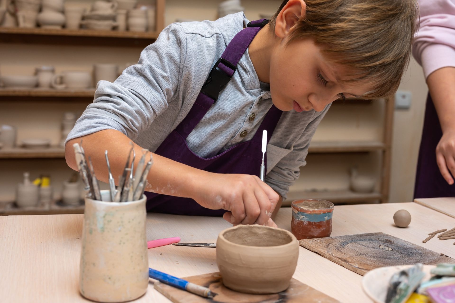 Child shaping clay at a pottery wheel with tools in a studio