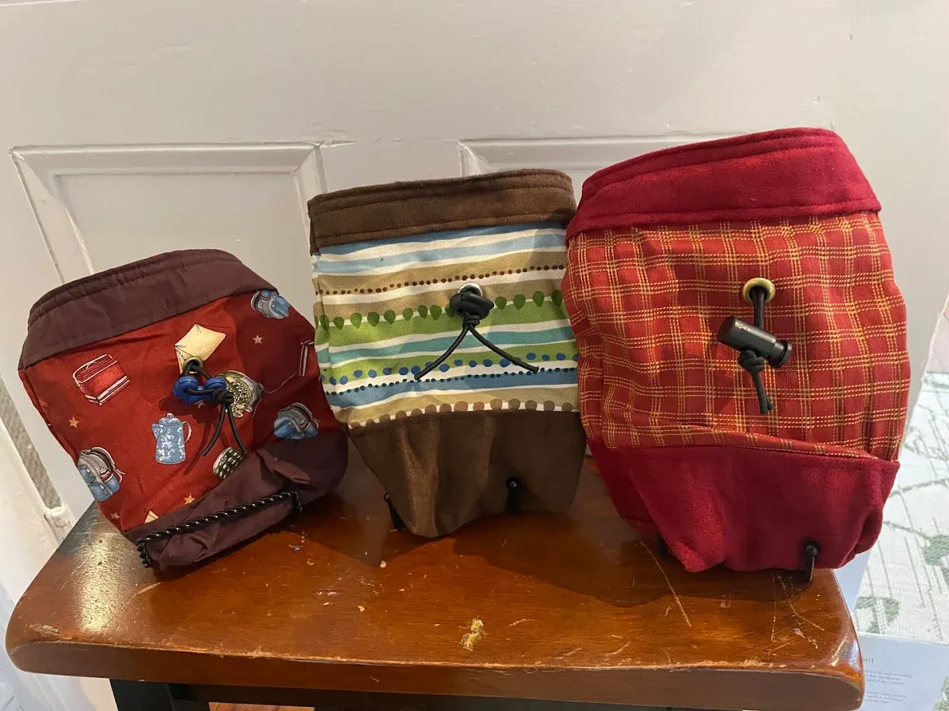 Three colorful fabric pouches with drawstrings sitting on a wooden bench