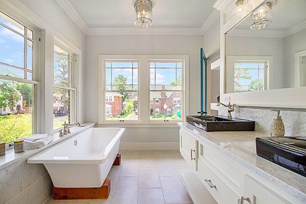 A bathroom with a tub , sink , mirror and two windows.