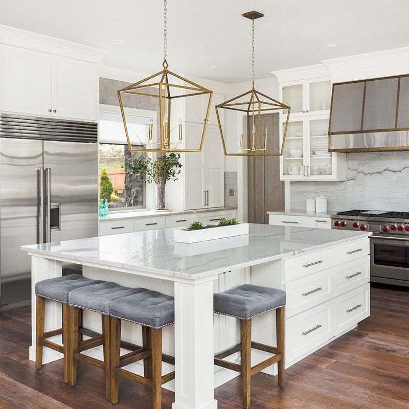 A kitchen with a large island , stools , a refrigerator and a stove.
