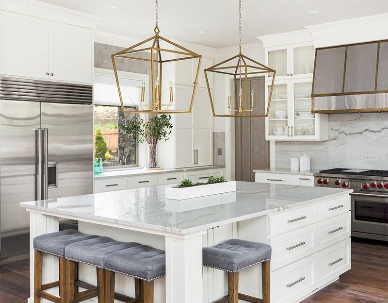 A kitchen with a large island , stools , a refrigerator and a stove.