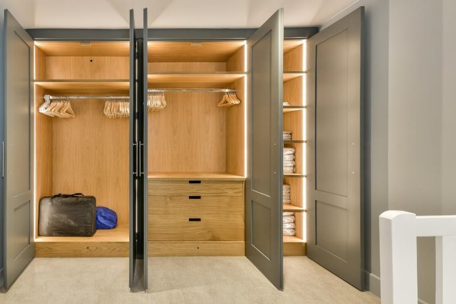 A walk in closet with the doors open and clothes in it