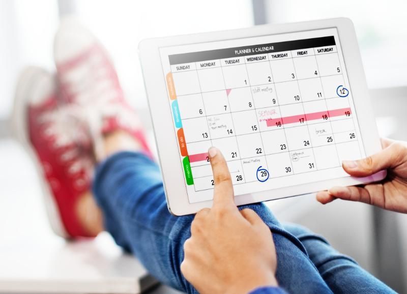 A person is holding a tablet with a calendar on it.