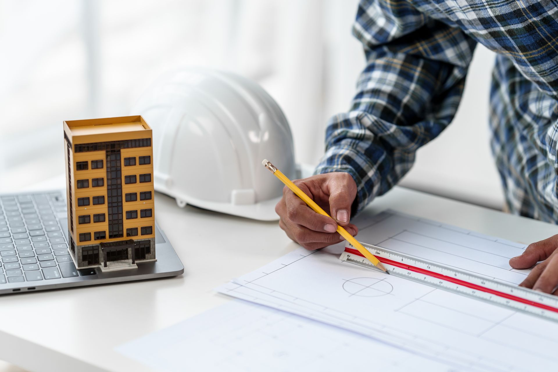 Architect reviewing building model and plans with pencil and hard hat on desk