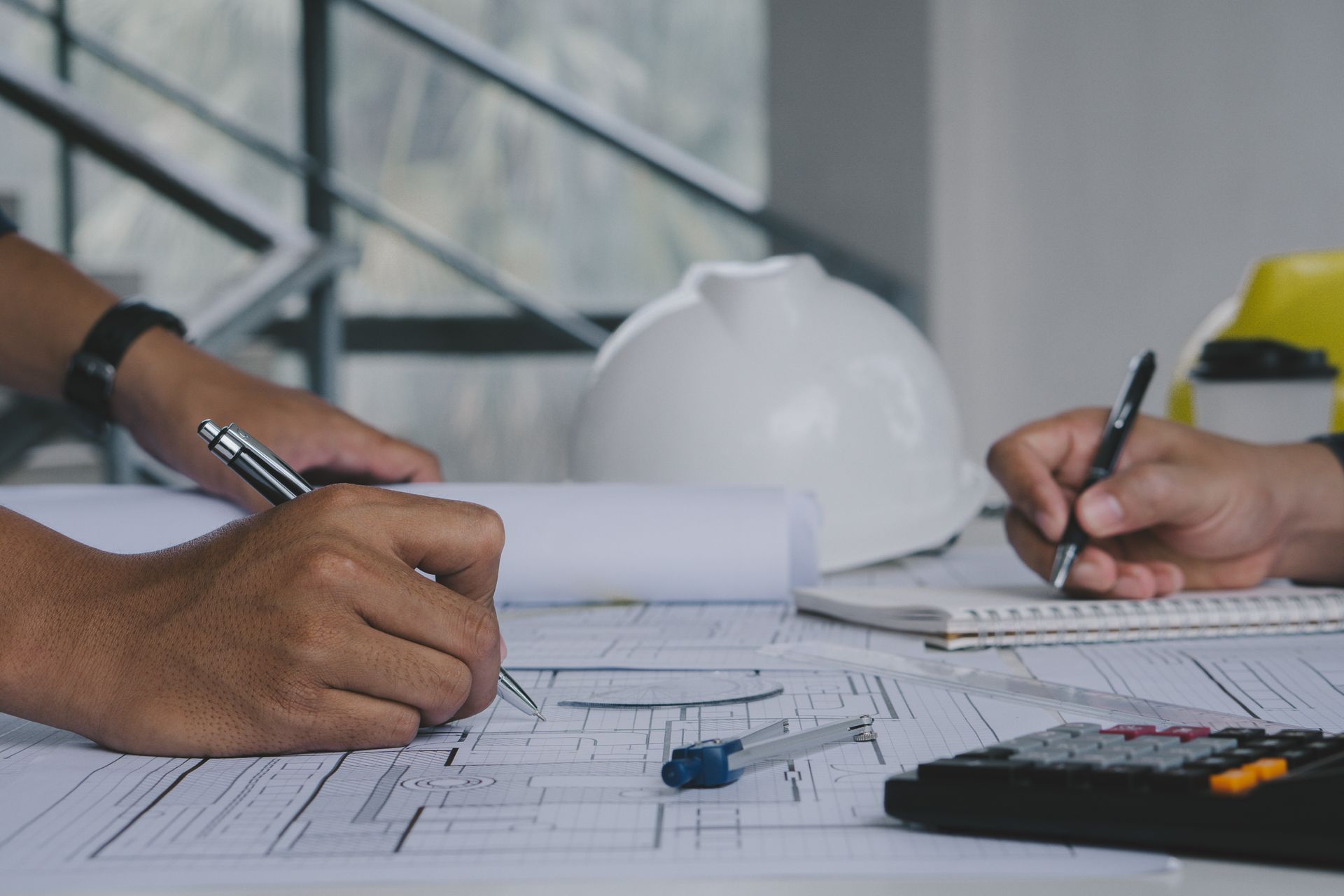 Two people reviewing blueprints at a desk with hard hats and drafting tools