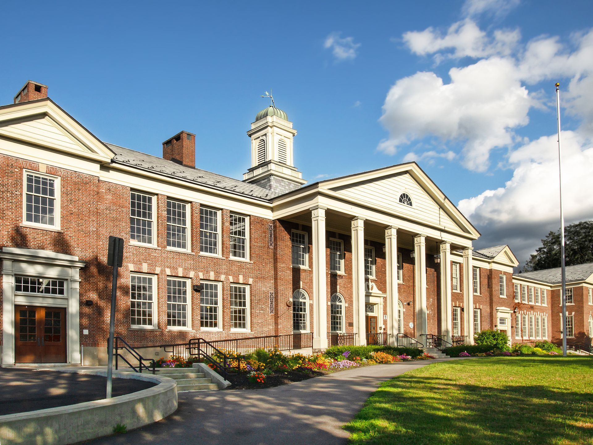 Brick civic building with white columns, red brick wings, and a clock tower on a sunny lawn