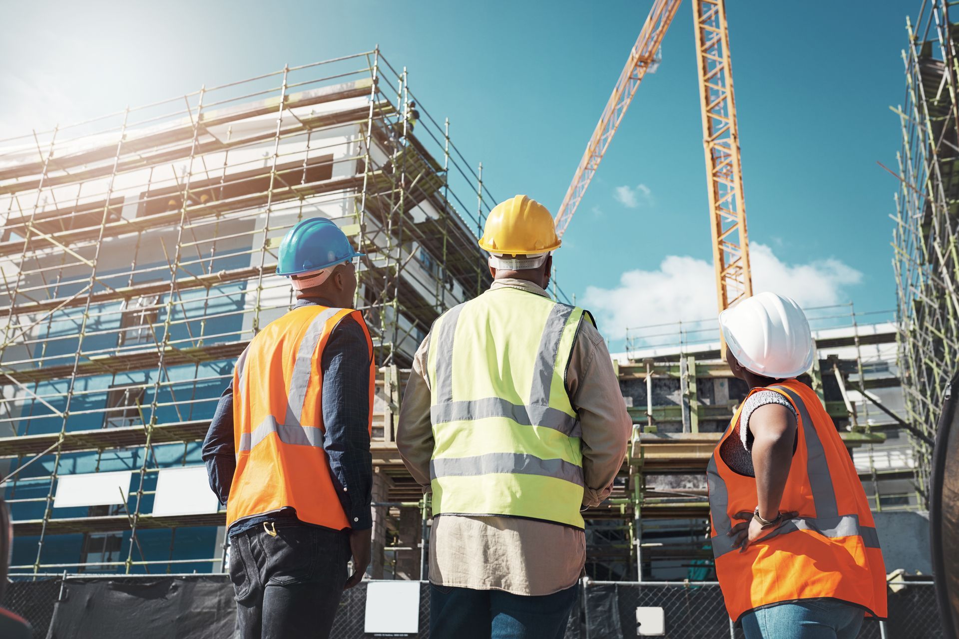 Construction workers in hard hats and vests at a building site with scaffolding and a crane