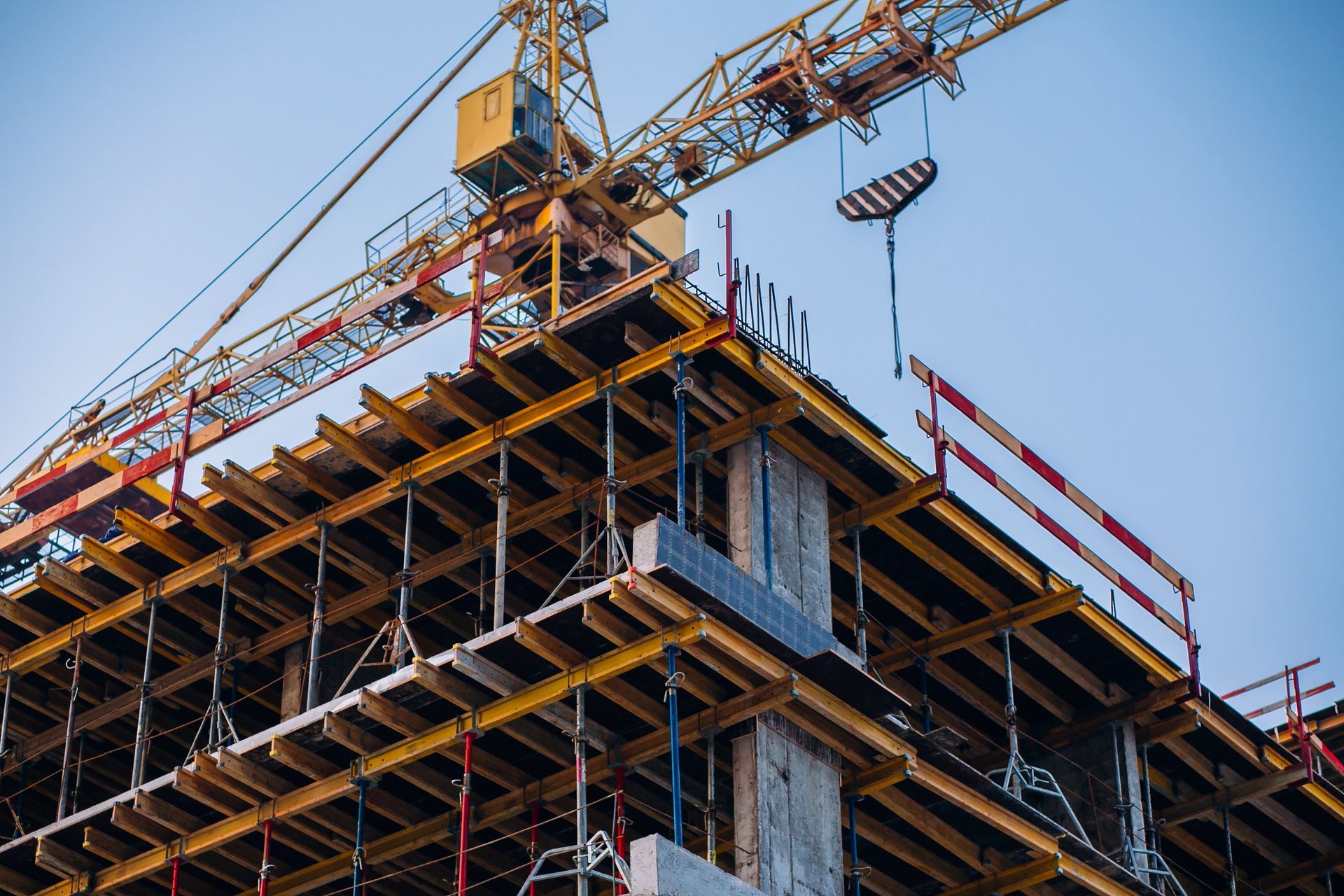 Construction site with a high-rise building framework, scaffolding, and a crane against a blue sky