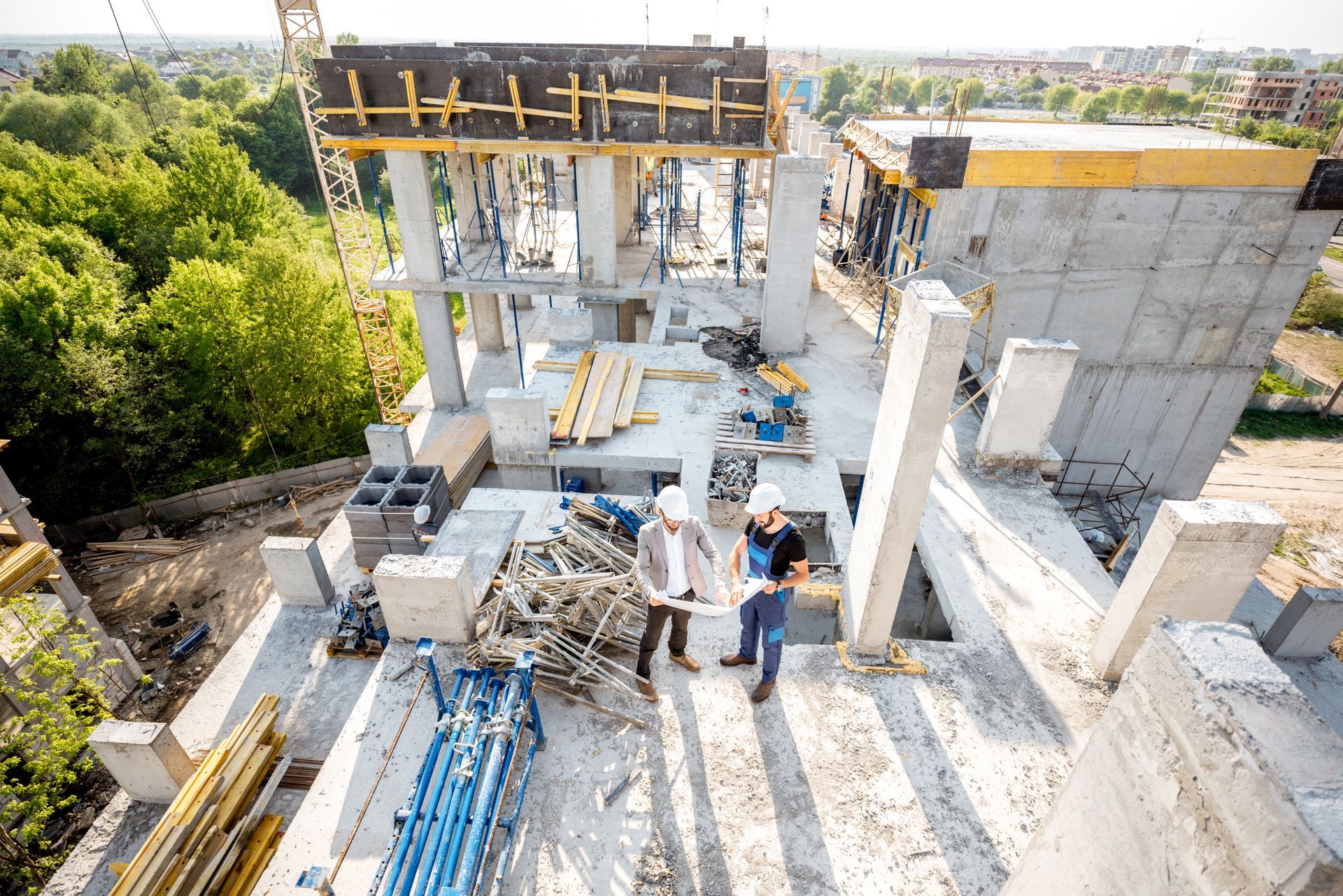 Construction workers on a building site with concrete walls, scaffolding, and stacked materials