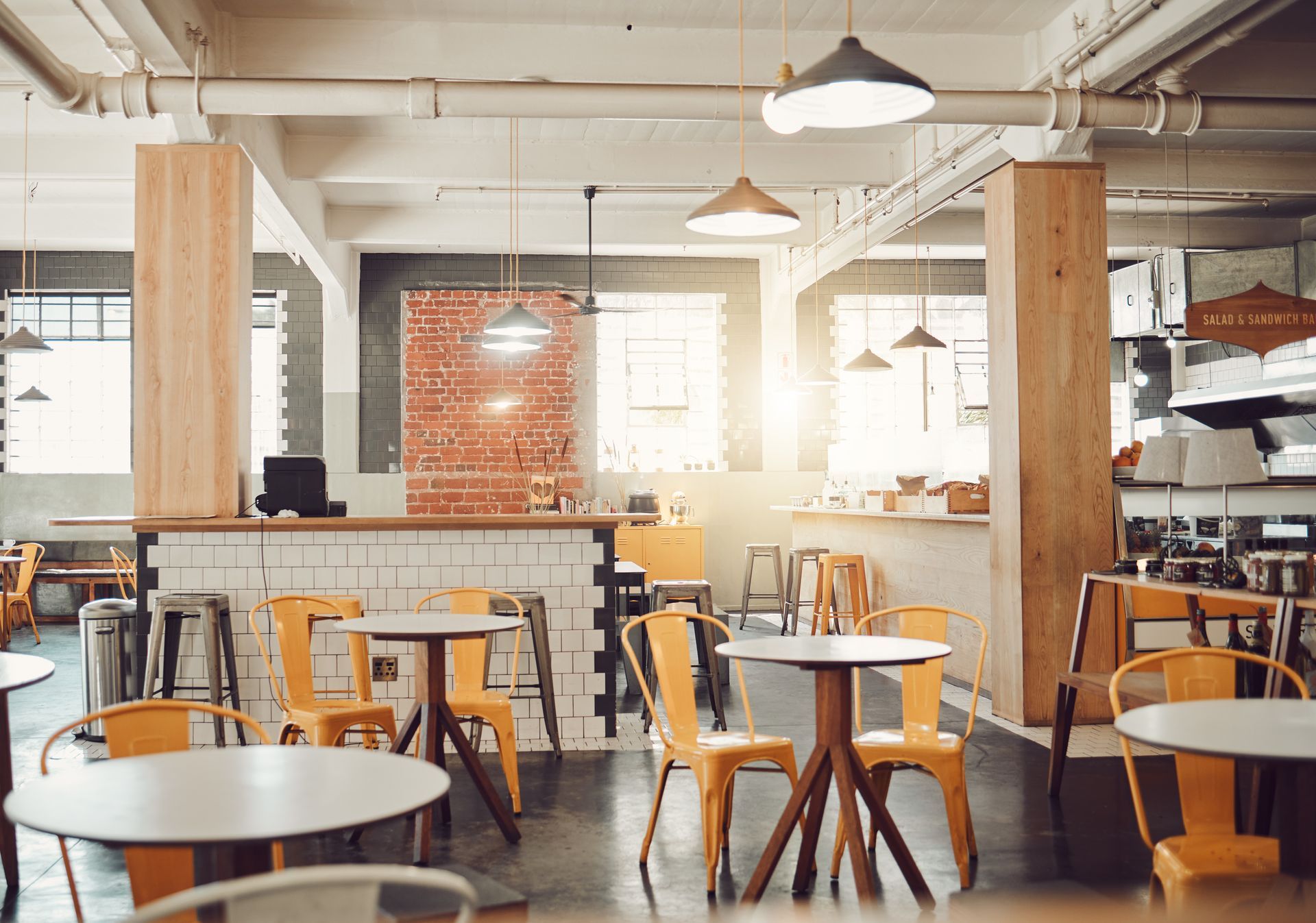 Bright, rustic café interior with wooden tables, stools, hanging lights, and large windows