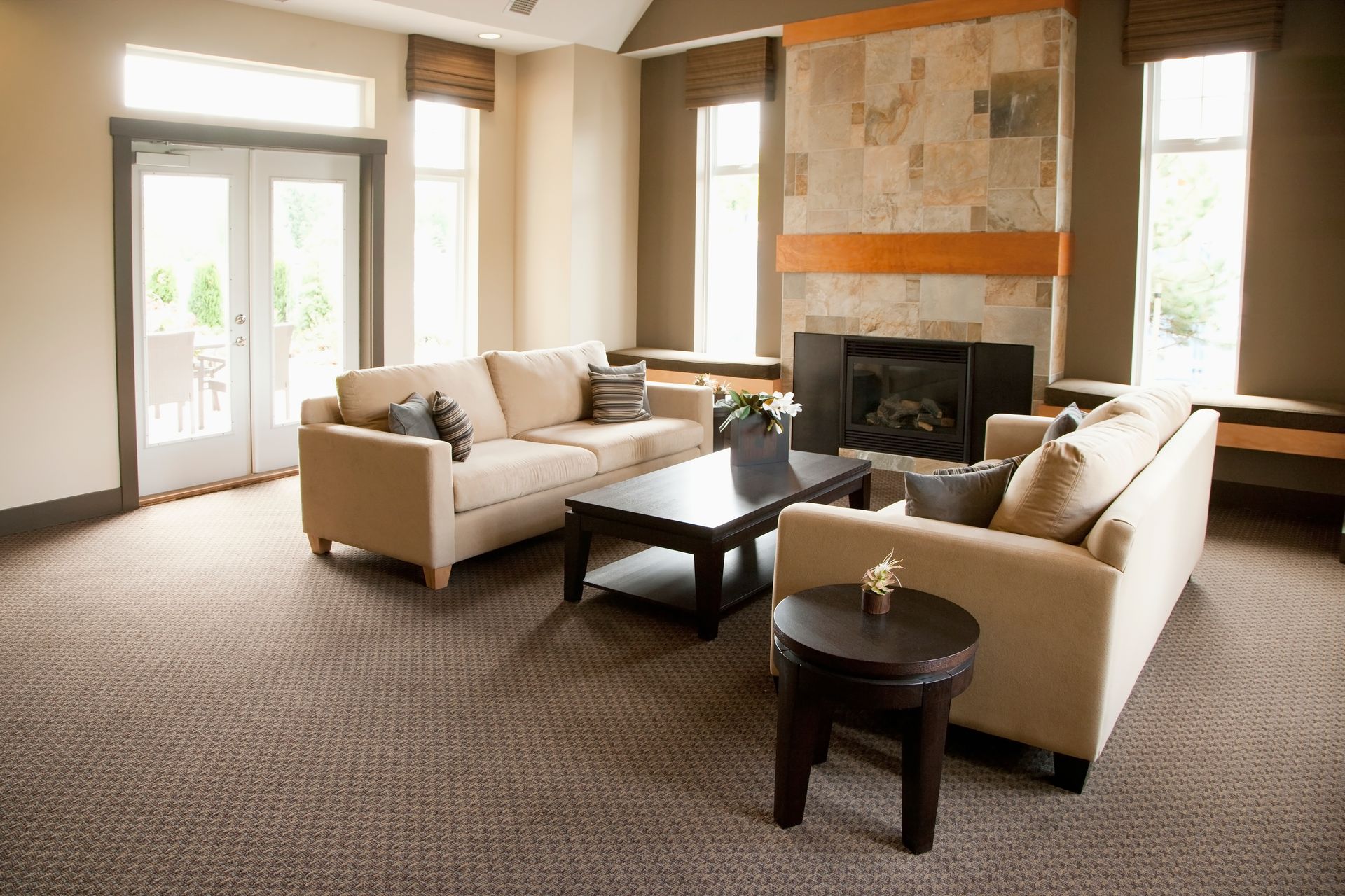Bright living room with beige sofas, a fireplace, coffee table, and large windows.