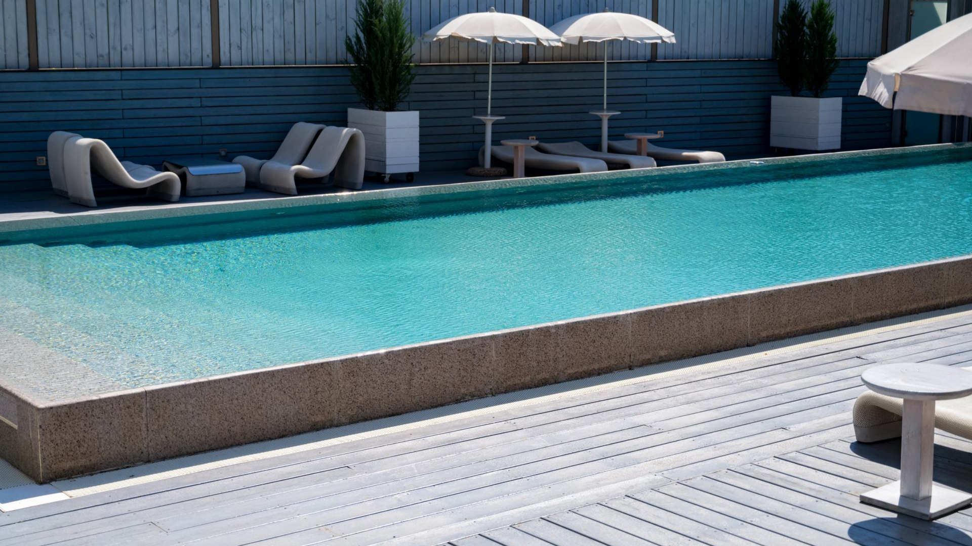 Long, rectangular turquoise pool with lounge chairs and umbrellas.