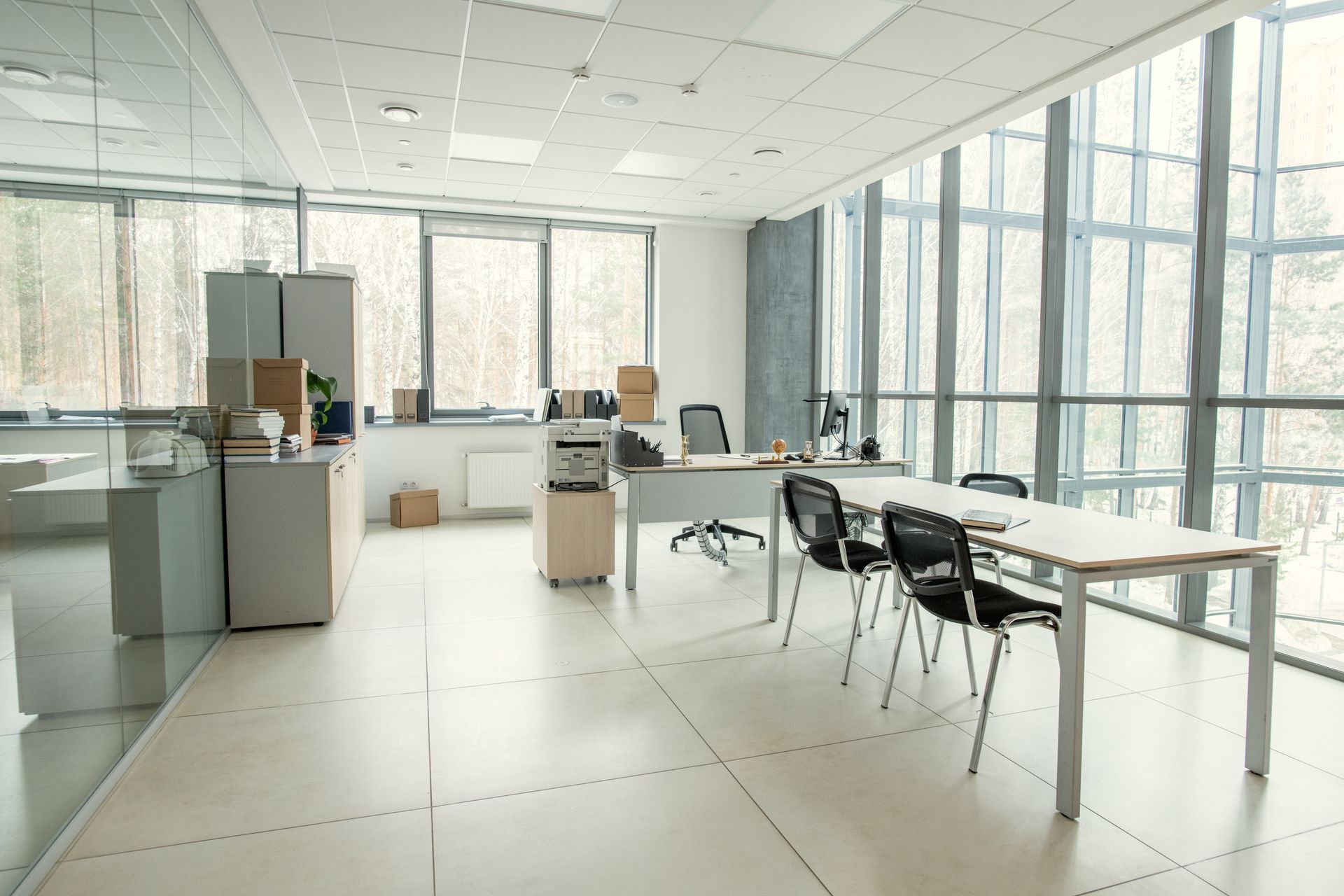 Bright, empty office with desks, chairs, boxes, and large windows letting in daylight