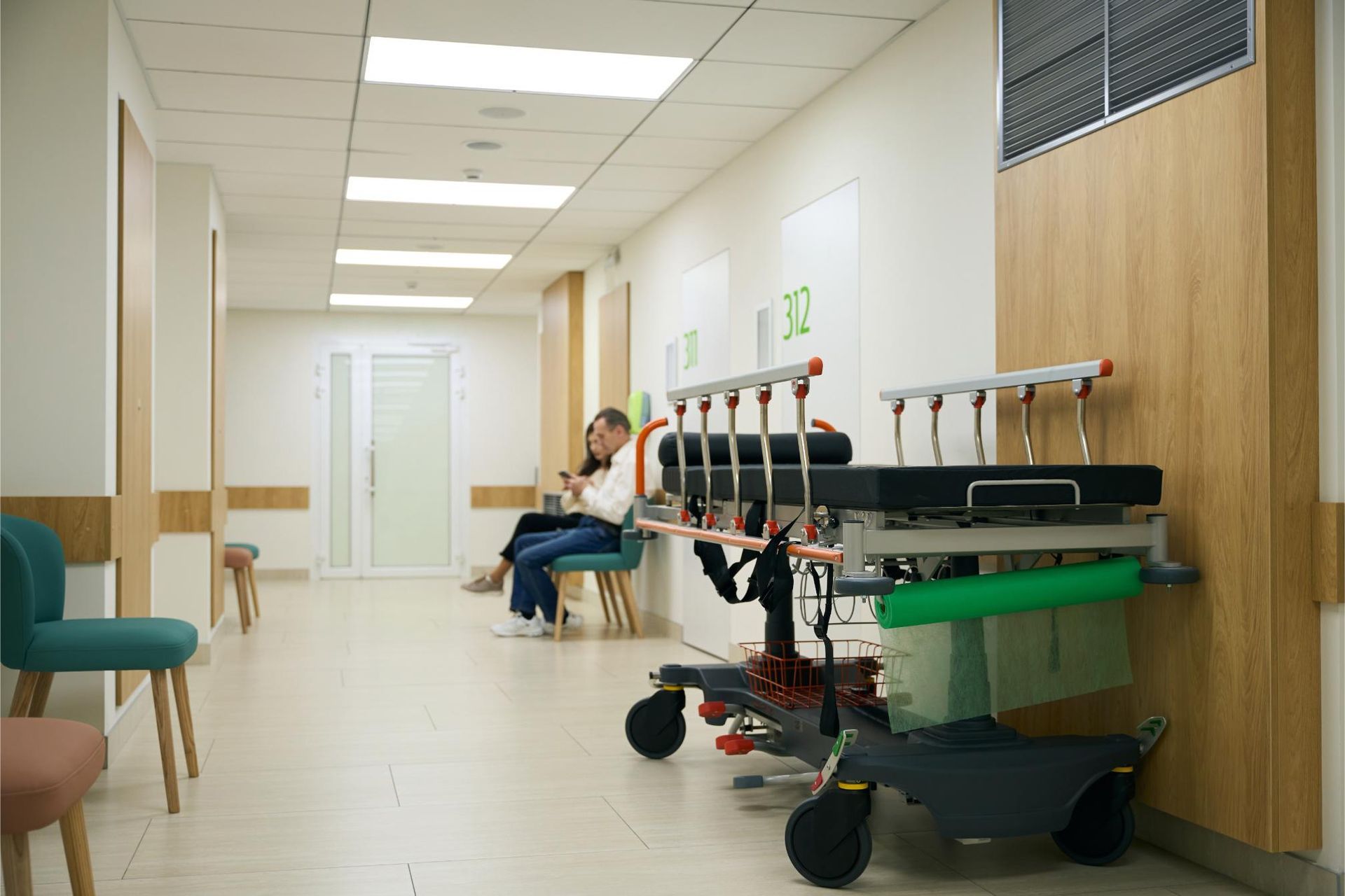 A person is sitting on a bench in a hospital hallway next to a stretcher.