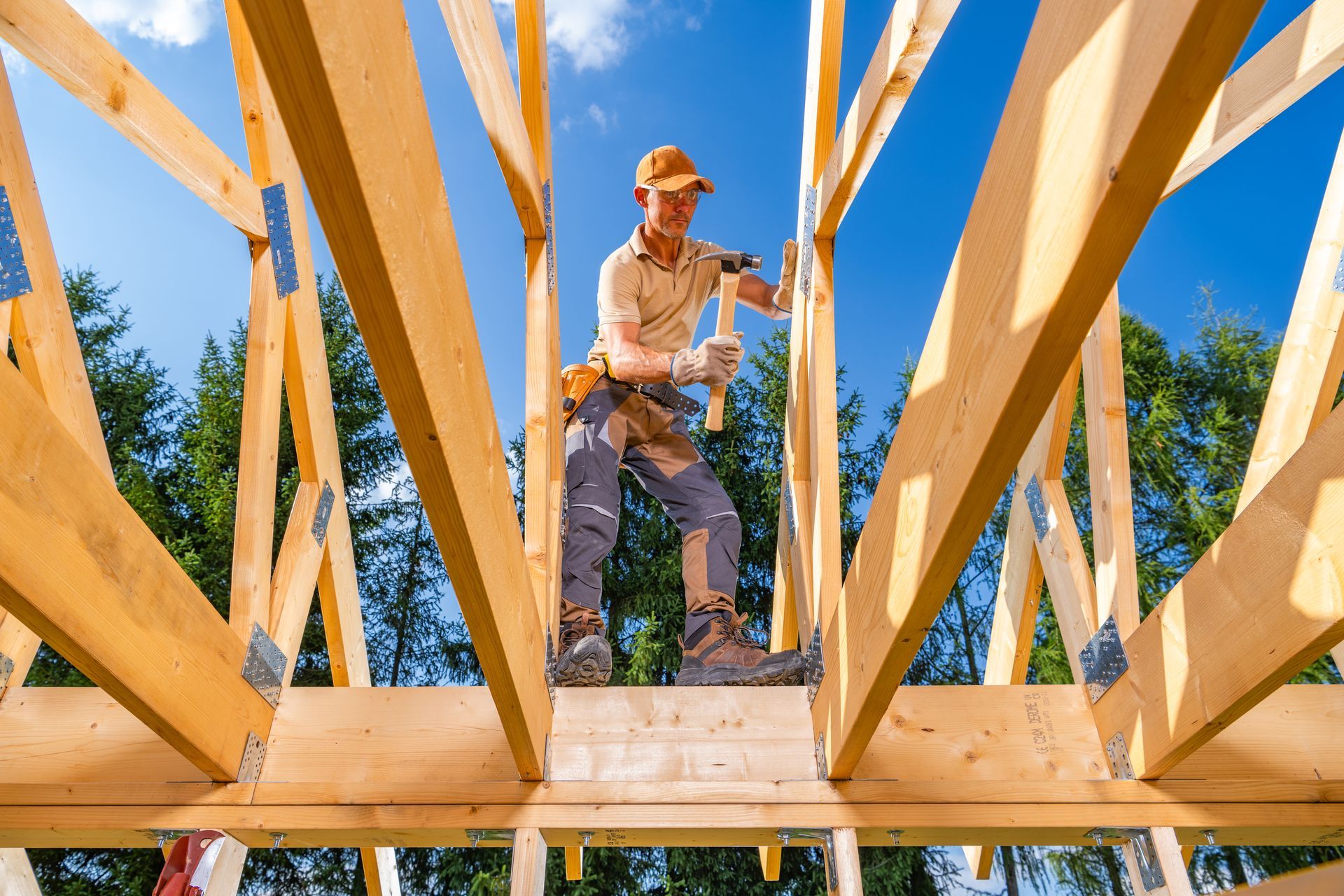Carpenter on rooftop frame, using a hammer, blue sky background.