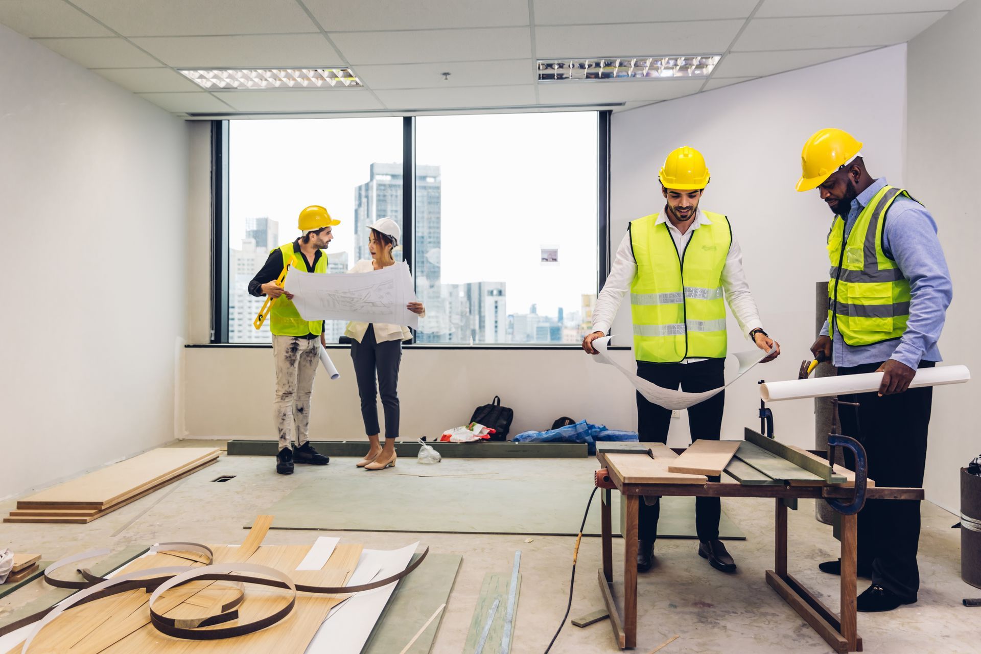 Construction workers reviewing blueprints in an unfinished office with tools and materials on the floor