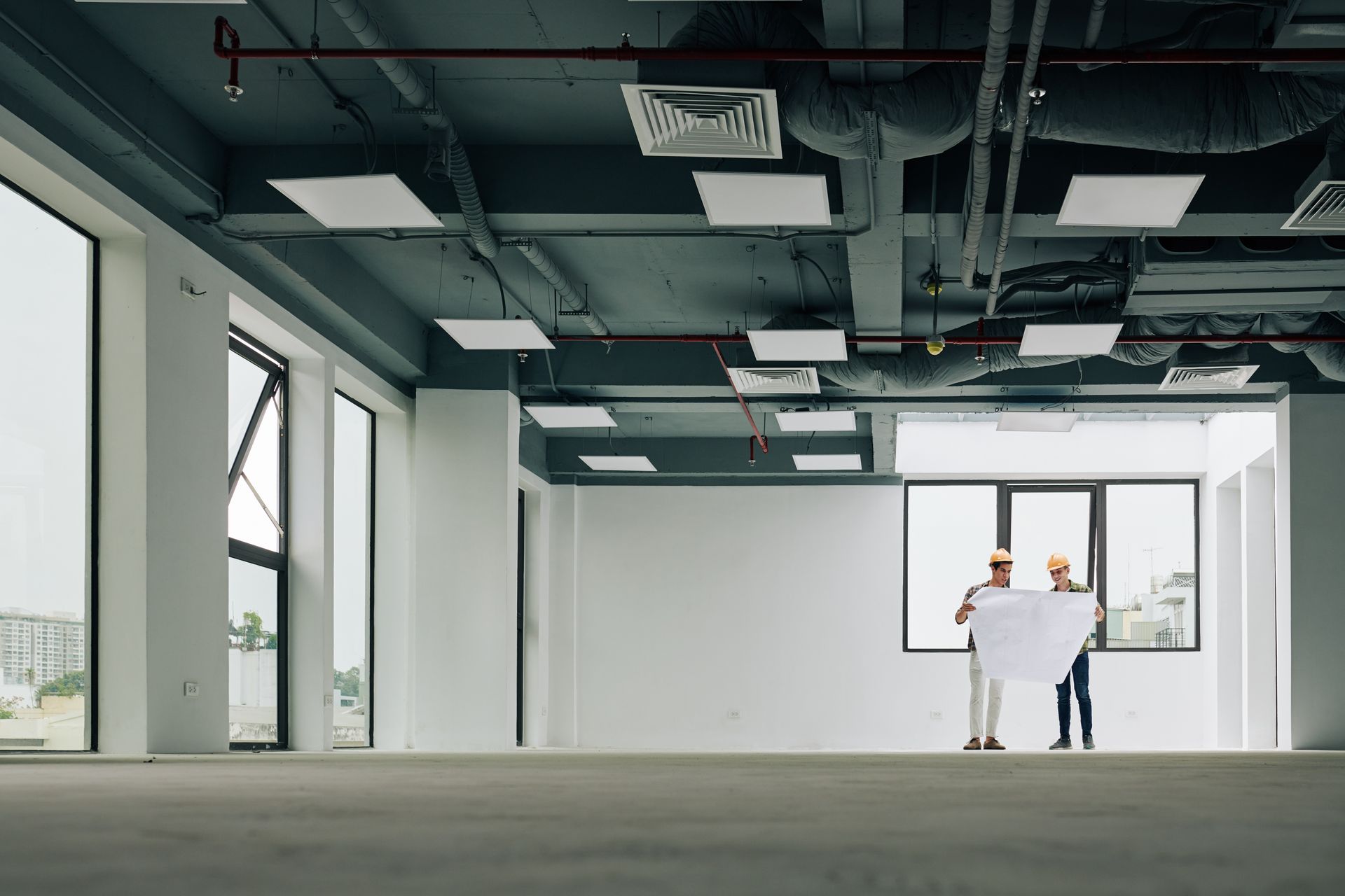 Two people holding a large white sheet in an empty modern office with floor-to-ceiling windows.