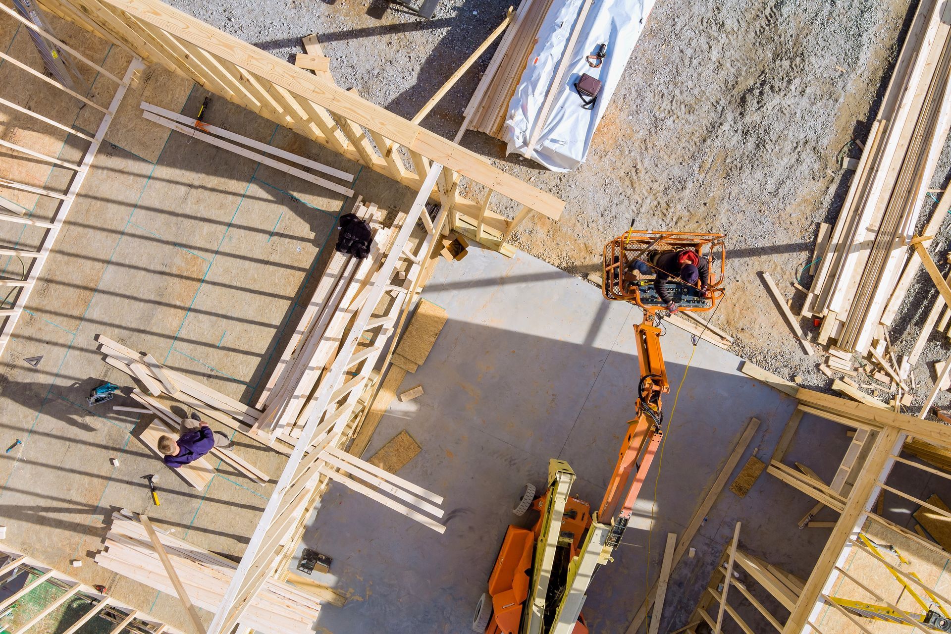 Aerial view of a construction site with workers, concrete walls, and an orange boom lift