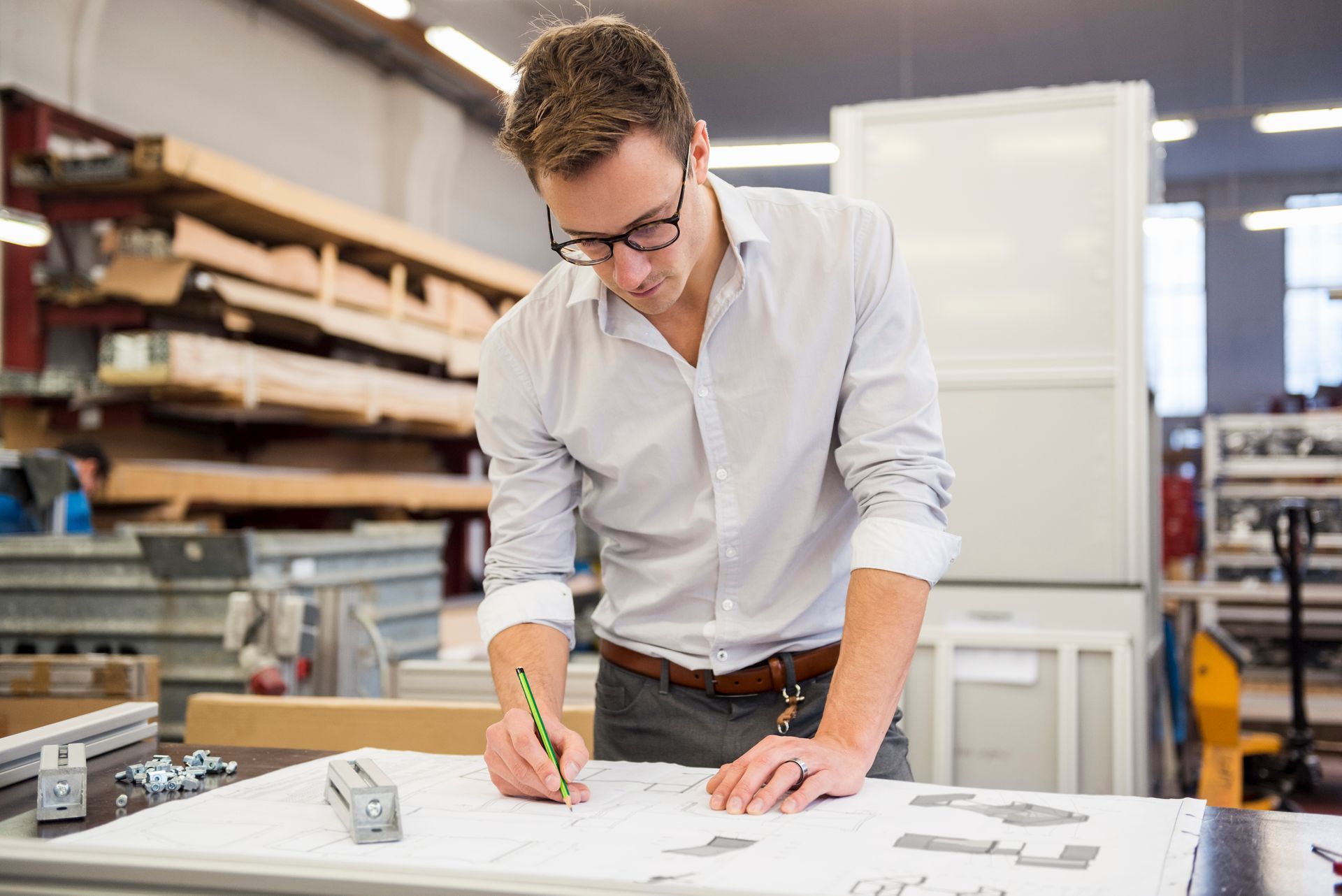 Designer sketching plans at a desk in a studio workspace with shelves and rolled materials behind him