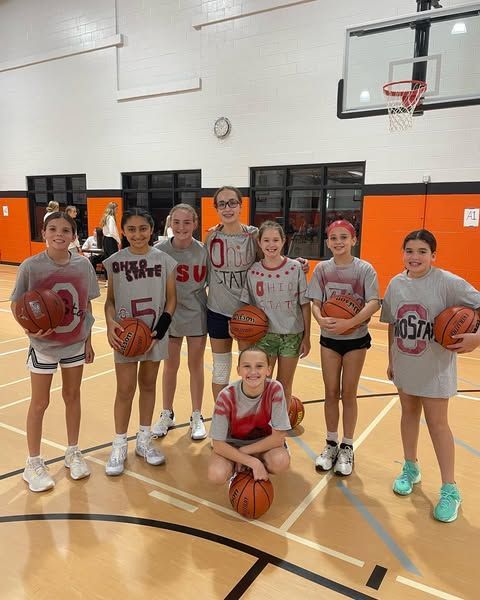 Youth basketball team posing in a gym, holding basketballs in front of a hoop.