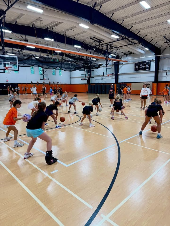 Students doing dribbling drills in a gymnasium with basketball hoops and orange cones
