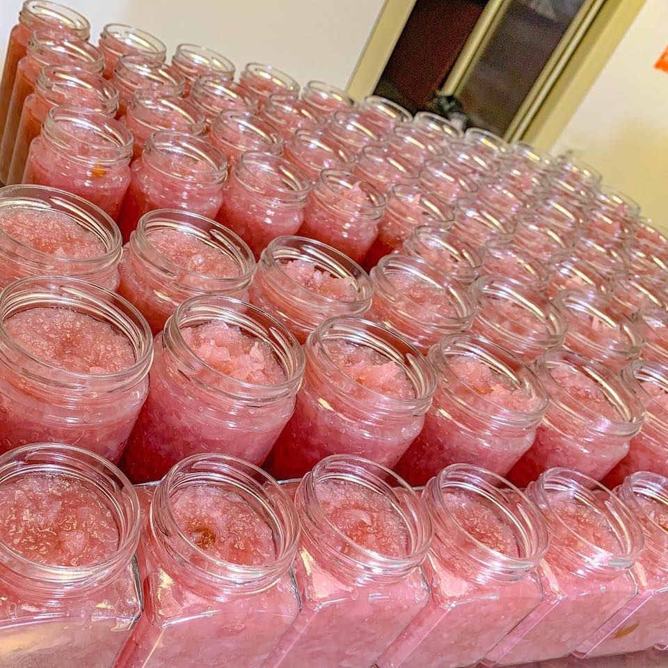 su un tavolo sono allineati un mucchio di barattoli pieni di liquido rosa.