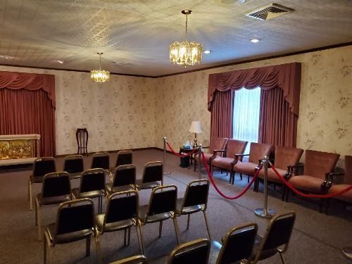 Small banquet room with rows of chairs, red curtains, chandeliers, and a roped-off stage area