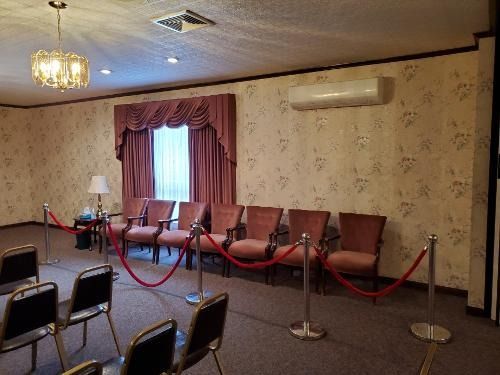 Empty meeting room with chairs, rope barriers, floral wallpaper, and a curtained window behind a long table