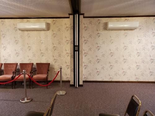 Empty lobby with patterned wallpaper, wall sconces, chairs, and red velvet rope barriers on carpet.